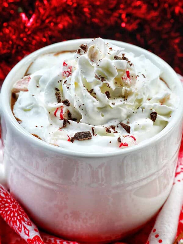 white mug with peppermint hot chocolate, whipped cream, surrounded by red and white Christmas decorations.