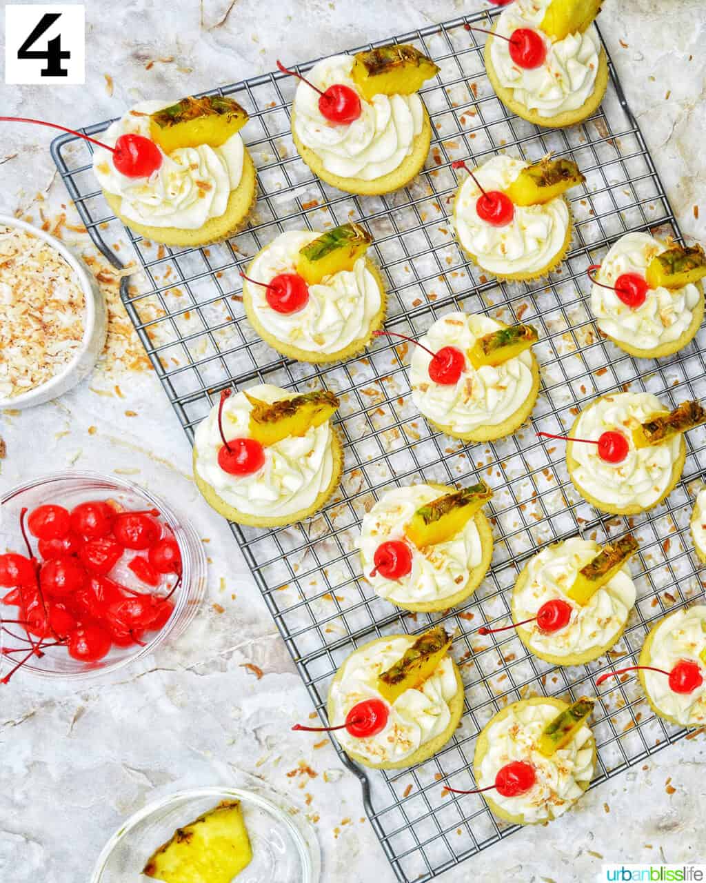 pina colada cupcakes frosted with lime slices and maraschino cherries on a wire rack.