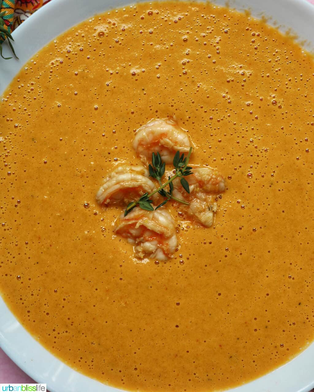 smooth silky shrimp and corn bisque in a bowl with fresh herbs and gold spoon.