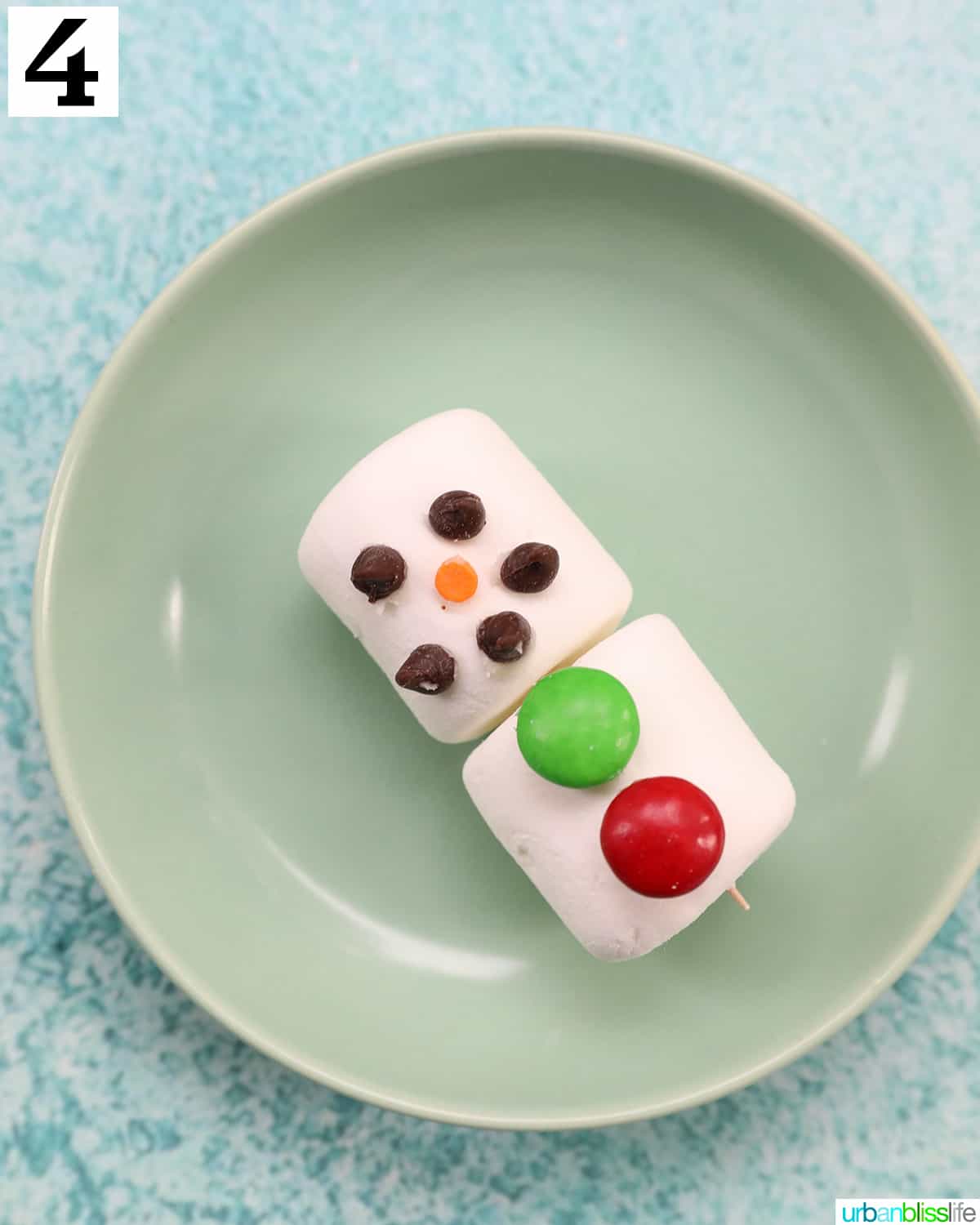 marshmallows with chocolate chips for eyes and mouth on a green plate.