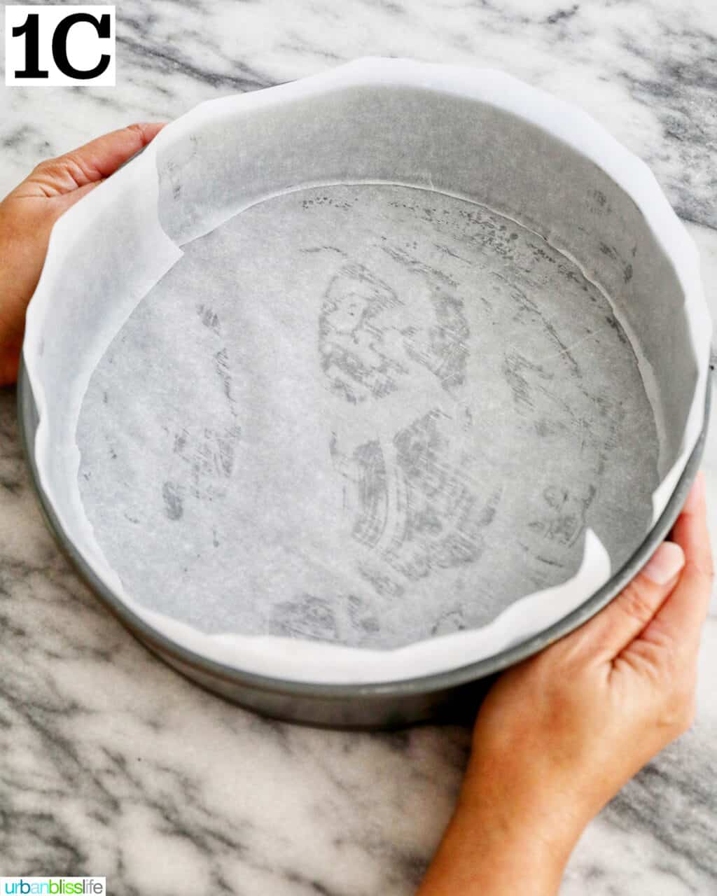 hands holding a springform pan lined with parchment paper.