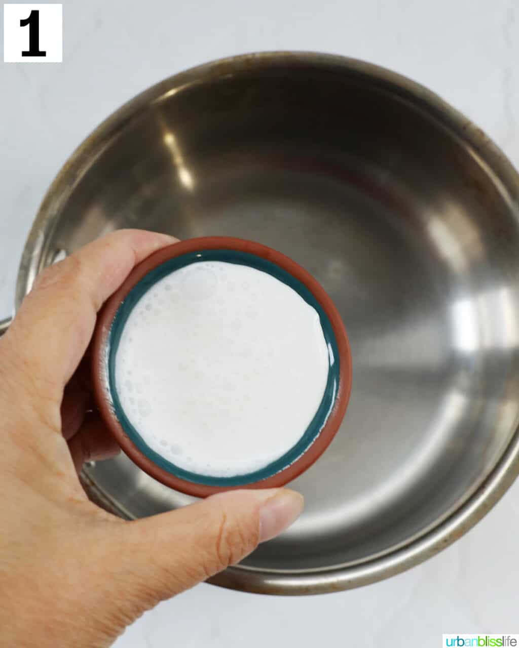 hand holding cream over a saucepan.