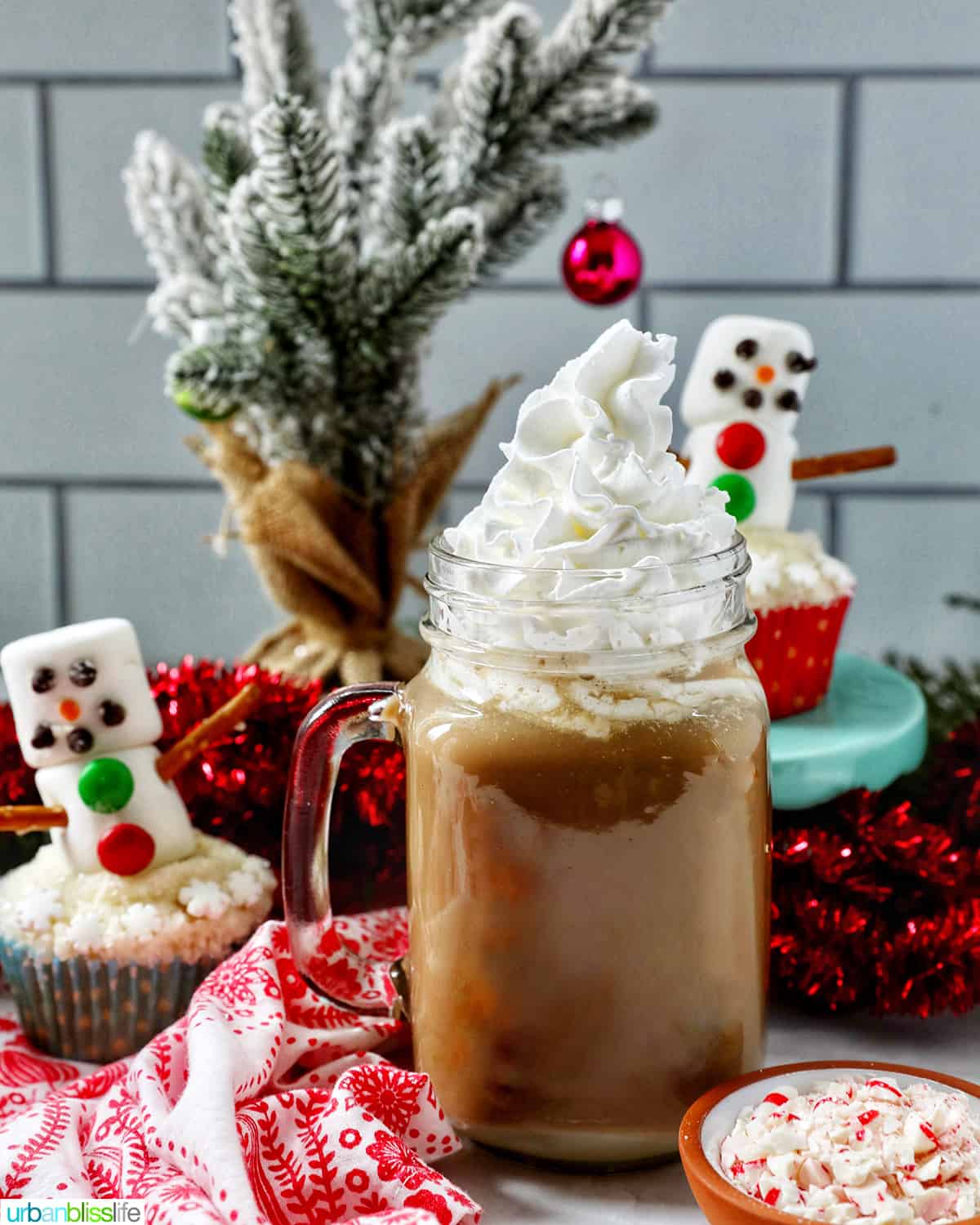 glass mug of white chocolate peppermint mocha with whipped cream with Christmas holiday decorations in the background.