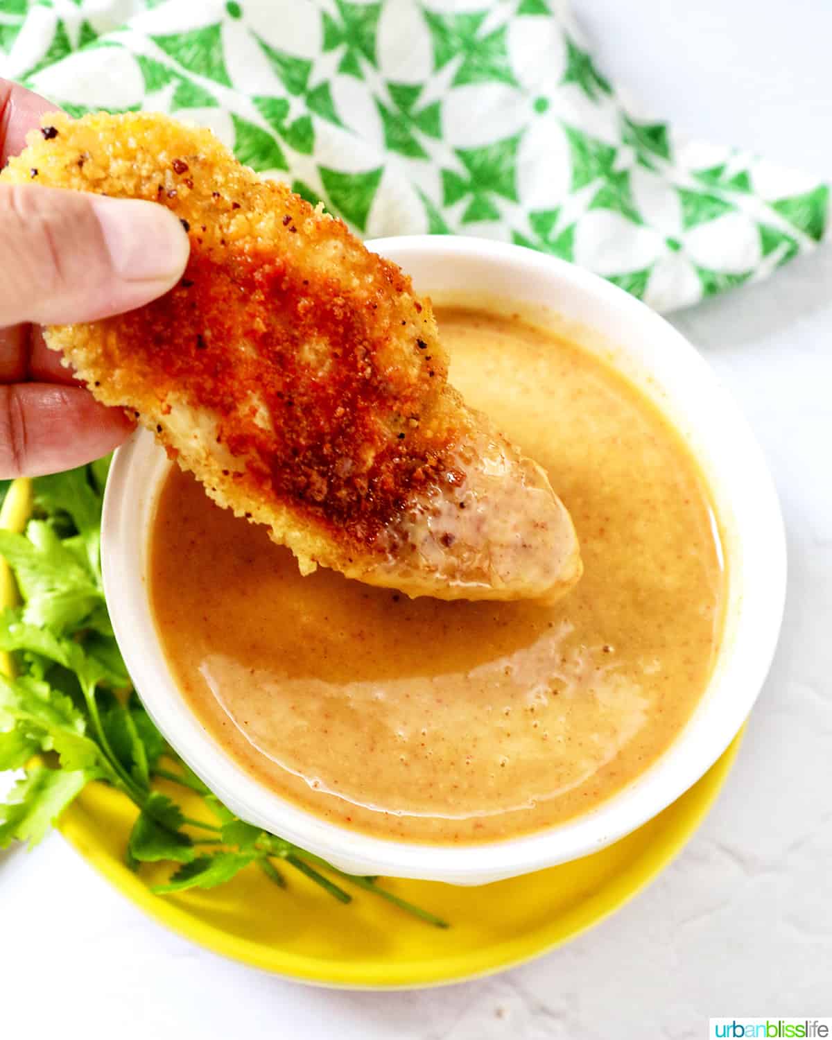 hand dipping a chicken tender into a bowl of honey mustard dipping sauce.