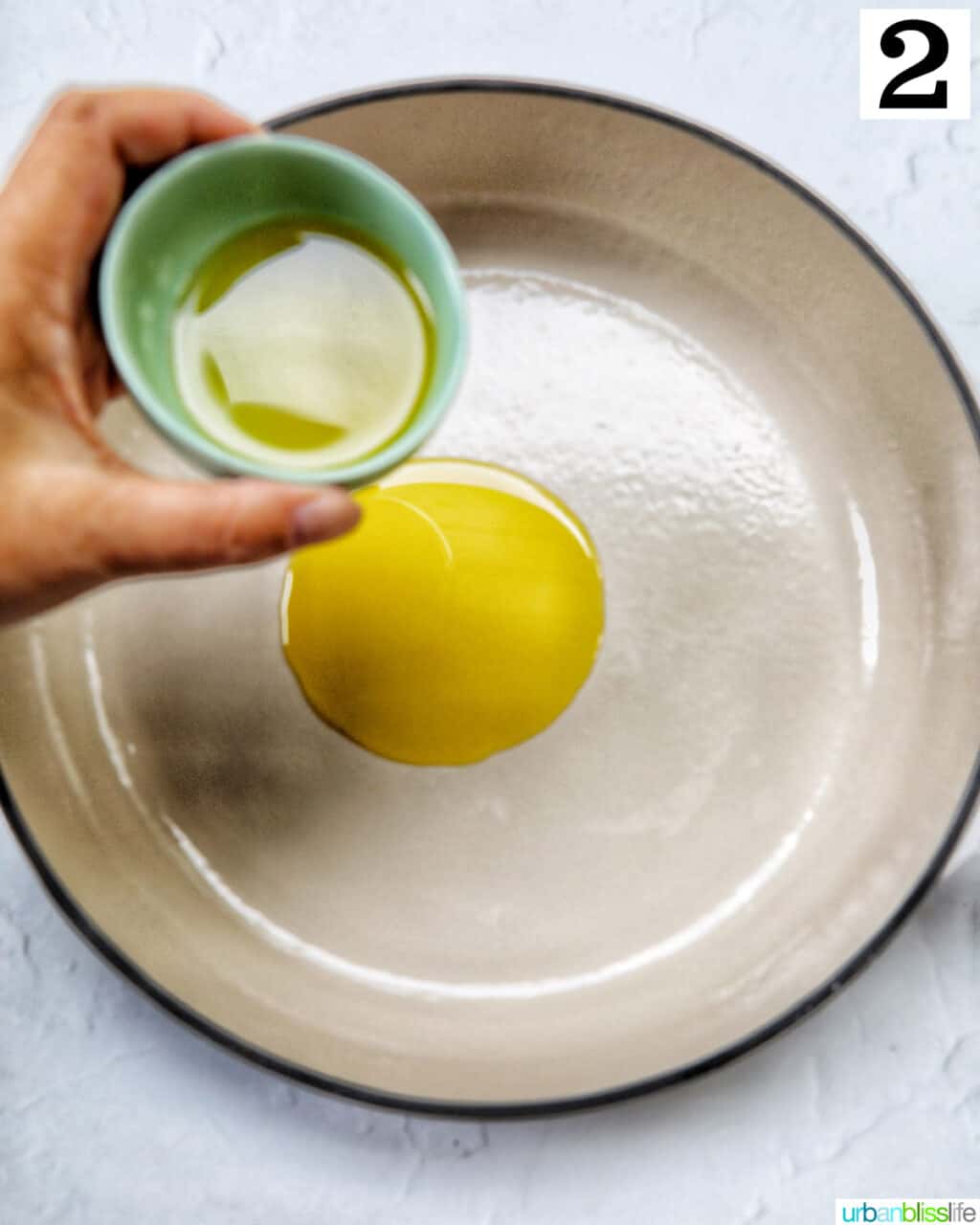 hand pouring olive oil into a large skillet.