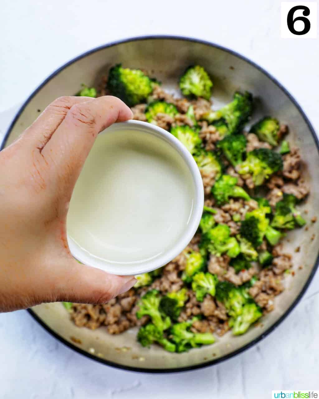 hand holding white wine over a large skillet of Italian sausage and broccoli.