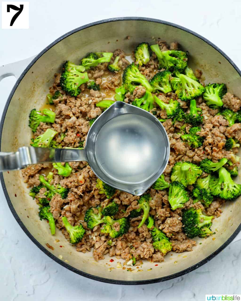 ladle with hot starchy pasta water over a large skillet of broccoli and Italian sausage.
