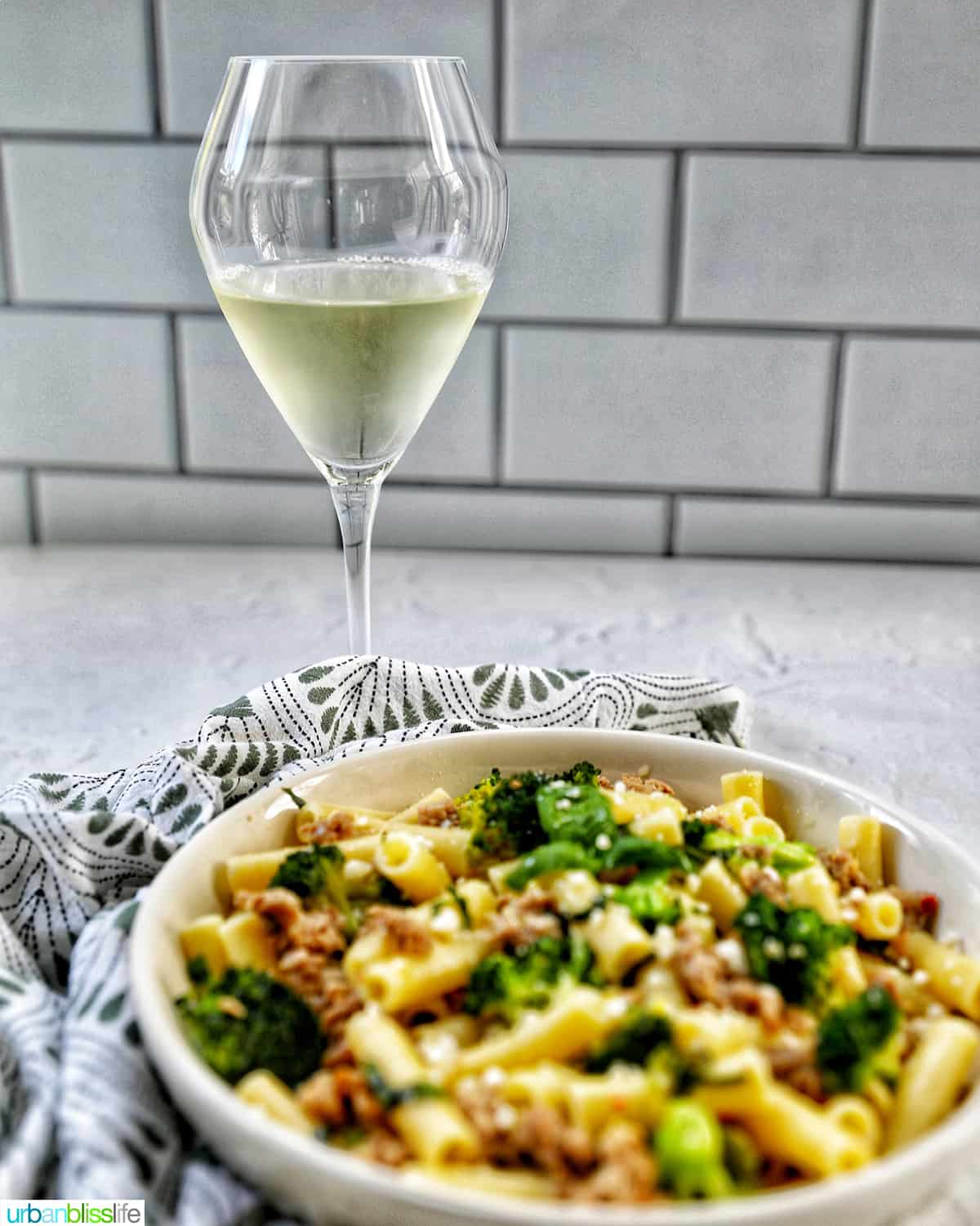 bowl of Italian Sausage and Broccoli pasta with a glass of white wine.