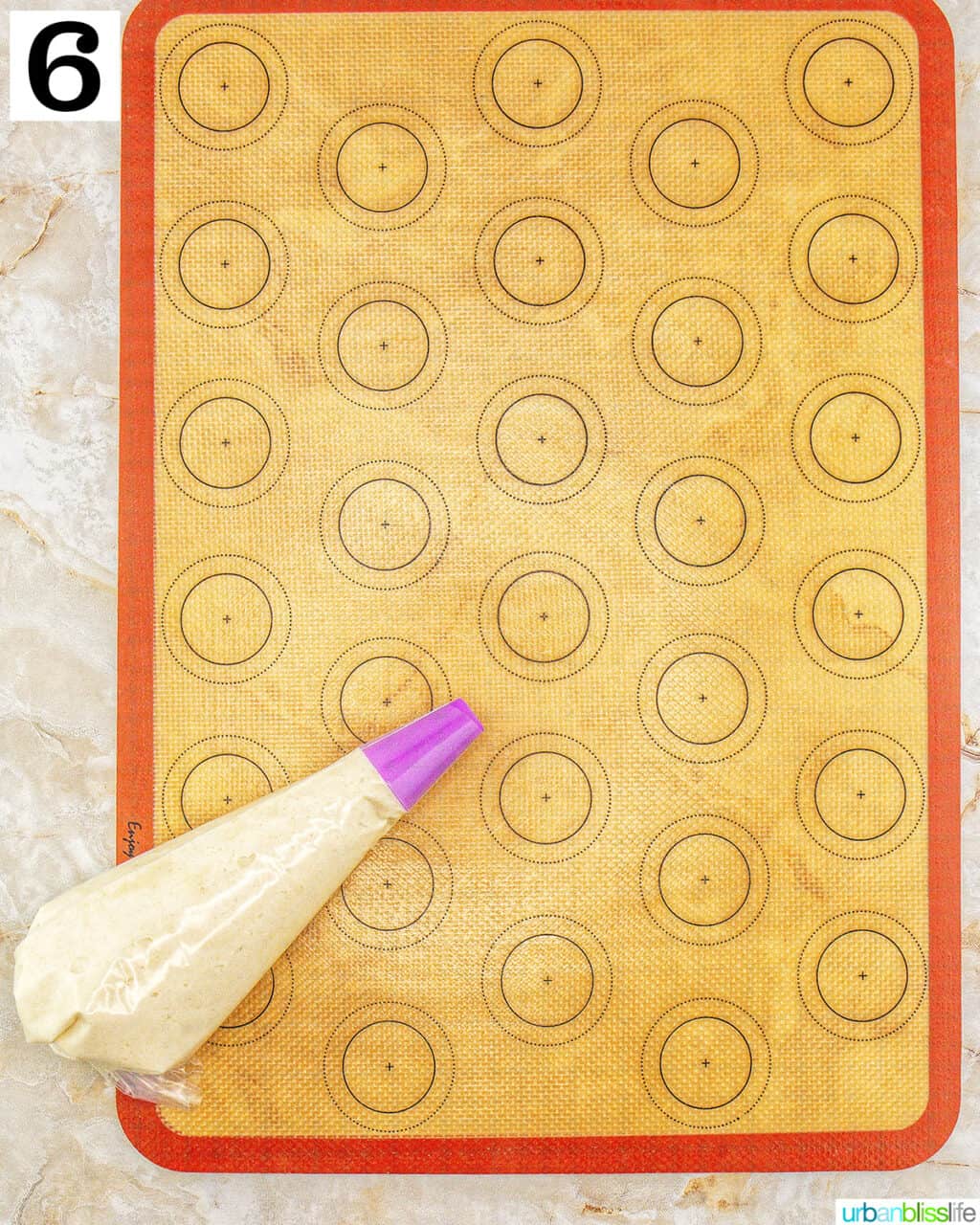 tiramisu macaron batter in a piping bag on top of a silicone macaron mat.