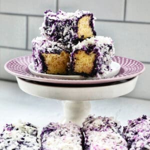 stack of ube bars sliced on a purple plated pedestal with a row of ube bars beneath.