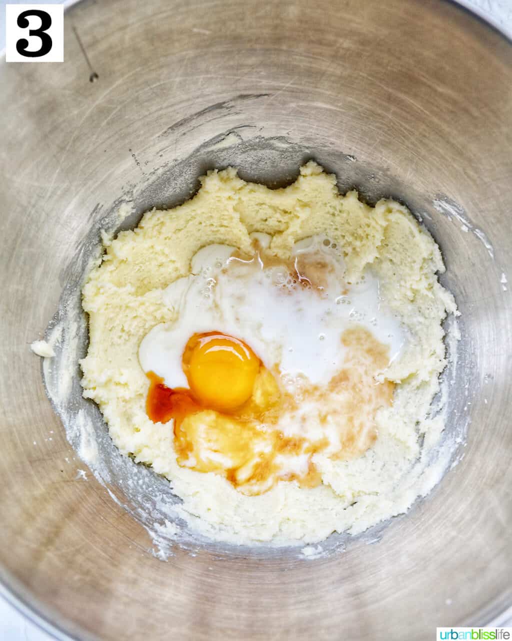 adding eggs and vanilla to butter and sugar in the stainless steel bowl of a stand mixer.