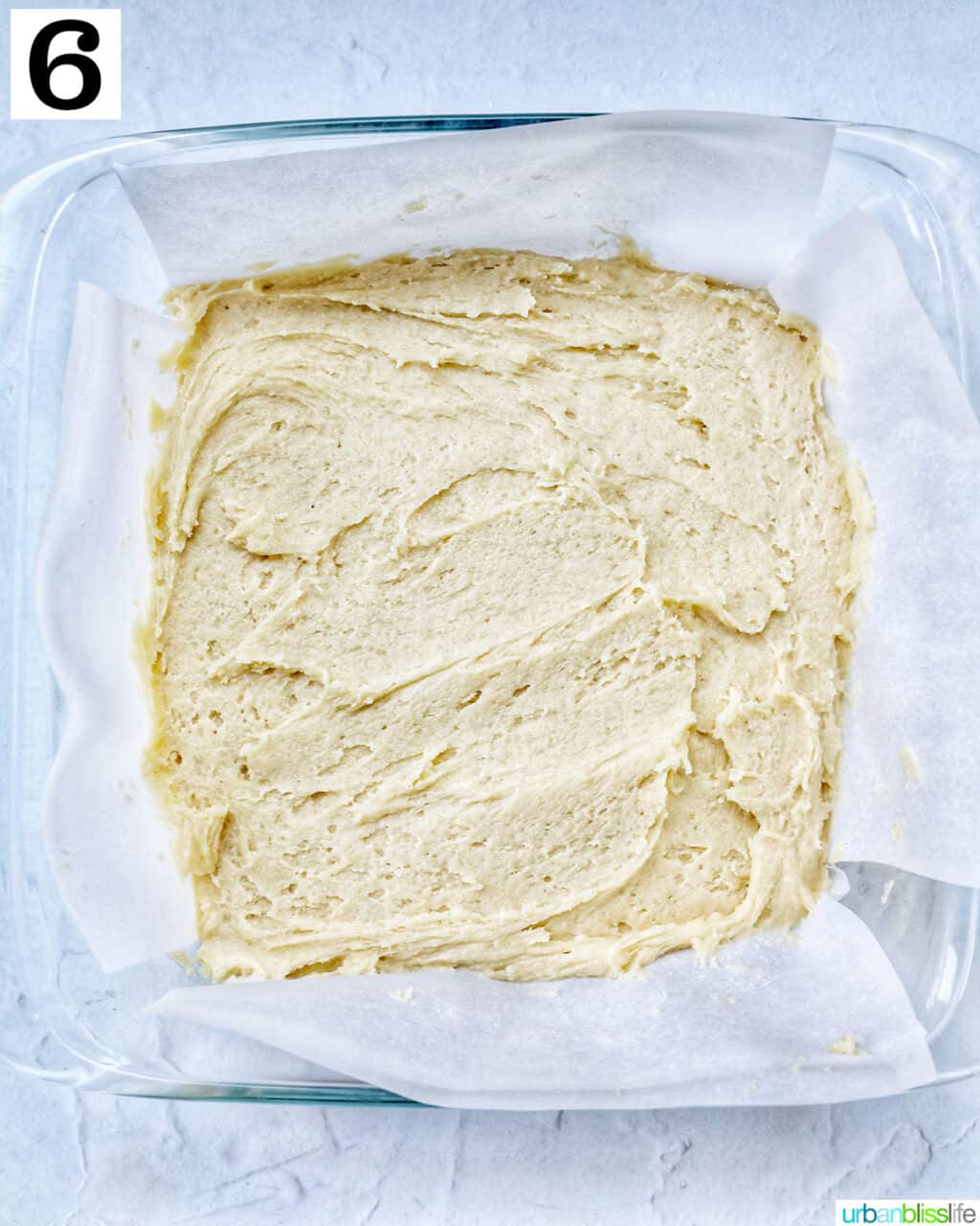 Thick cake batter in a glass baking dish lined with parchment paper.