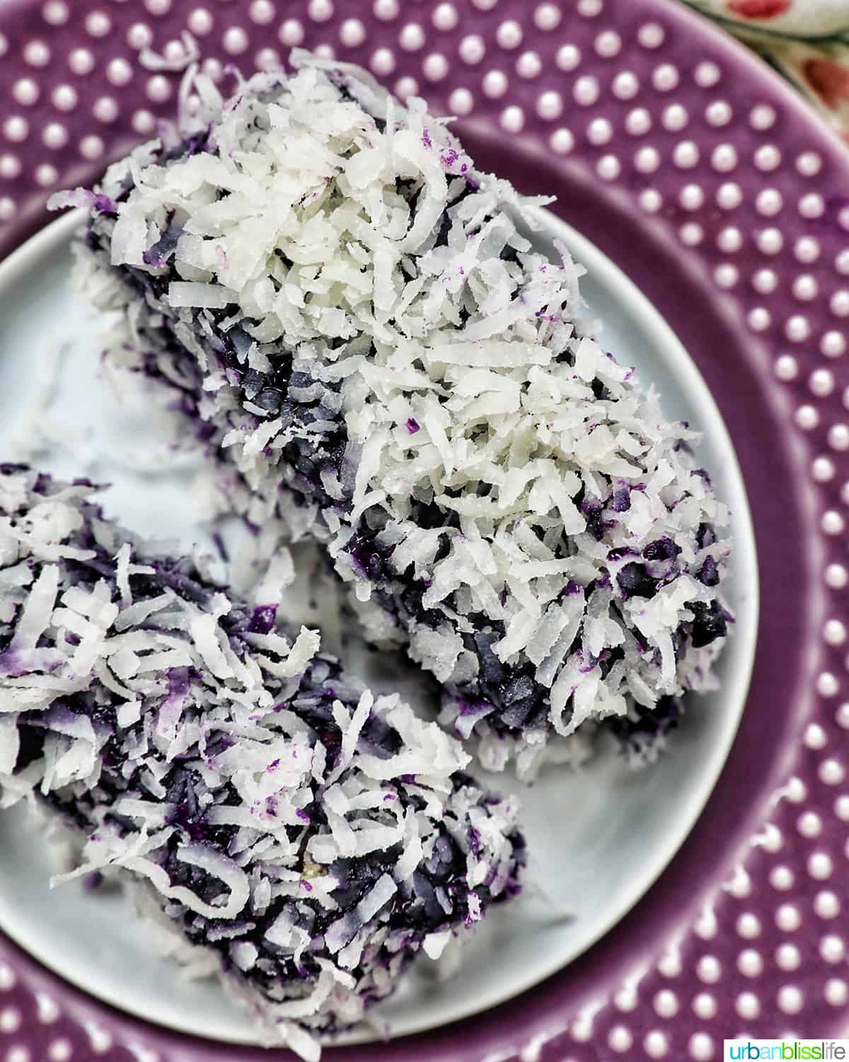 two ube cake bars covered in shredded coconut on a purple plate.