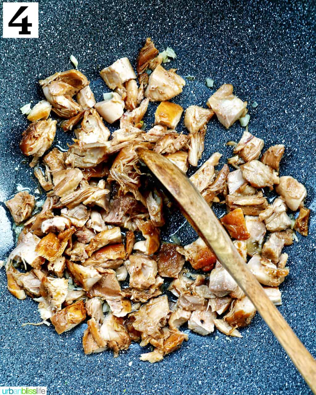 wooden spoon stirring adobo chicken in a wok.