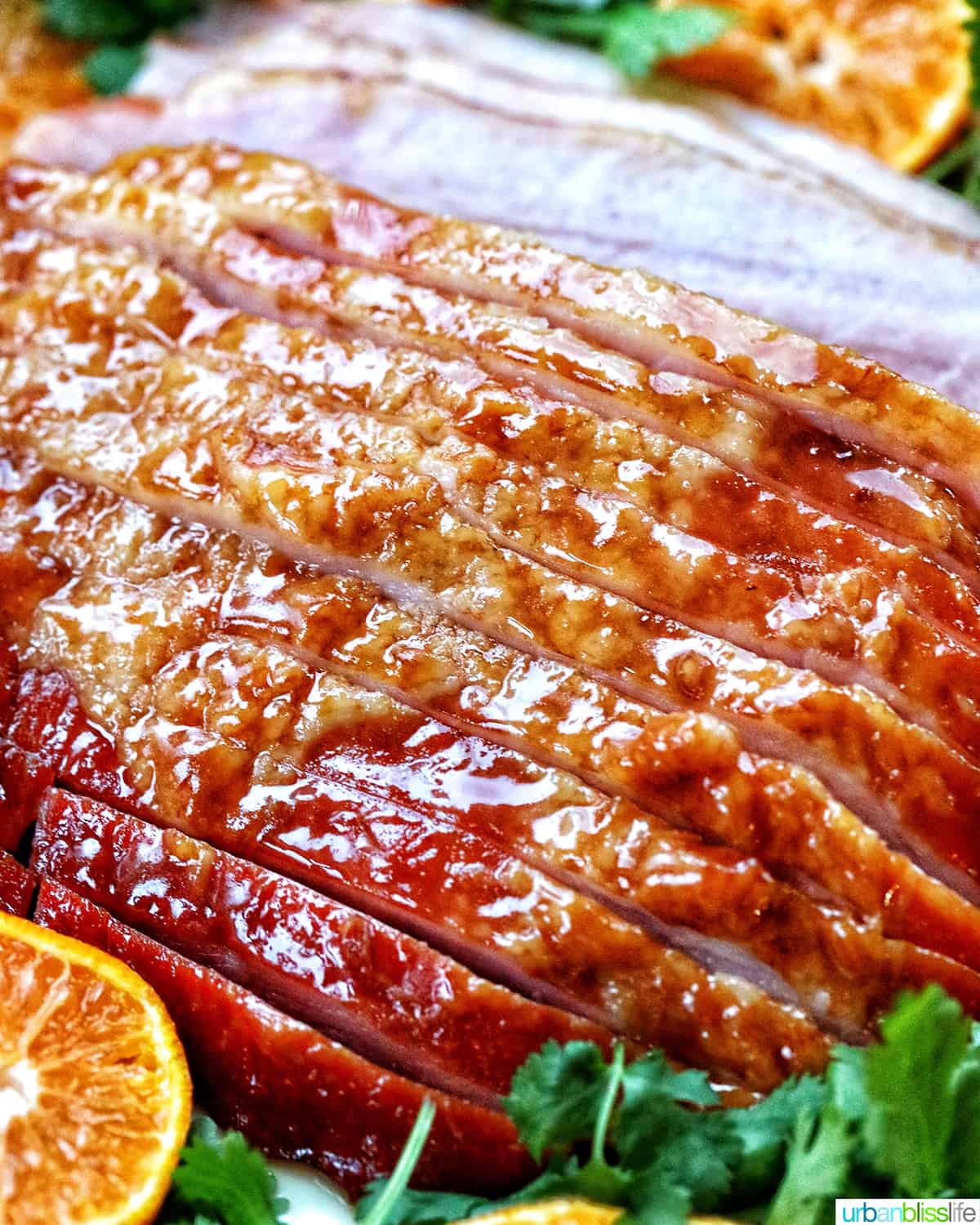 sliced honey glazed air fryer ham on a plate with fresh herbs and sliced oranges.