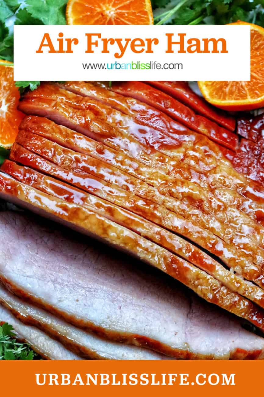 sliced honey glazed air fryer ham on a plate with fresh herbs and sliced oranges and title text overlay.
