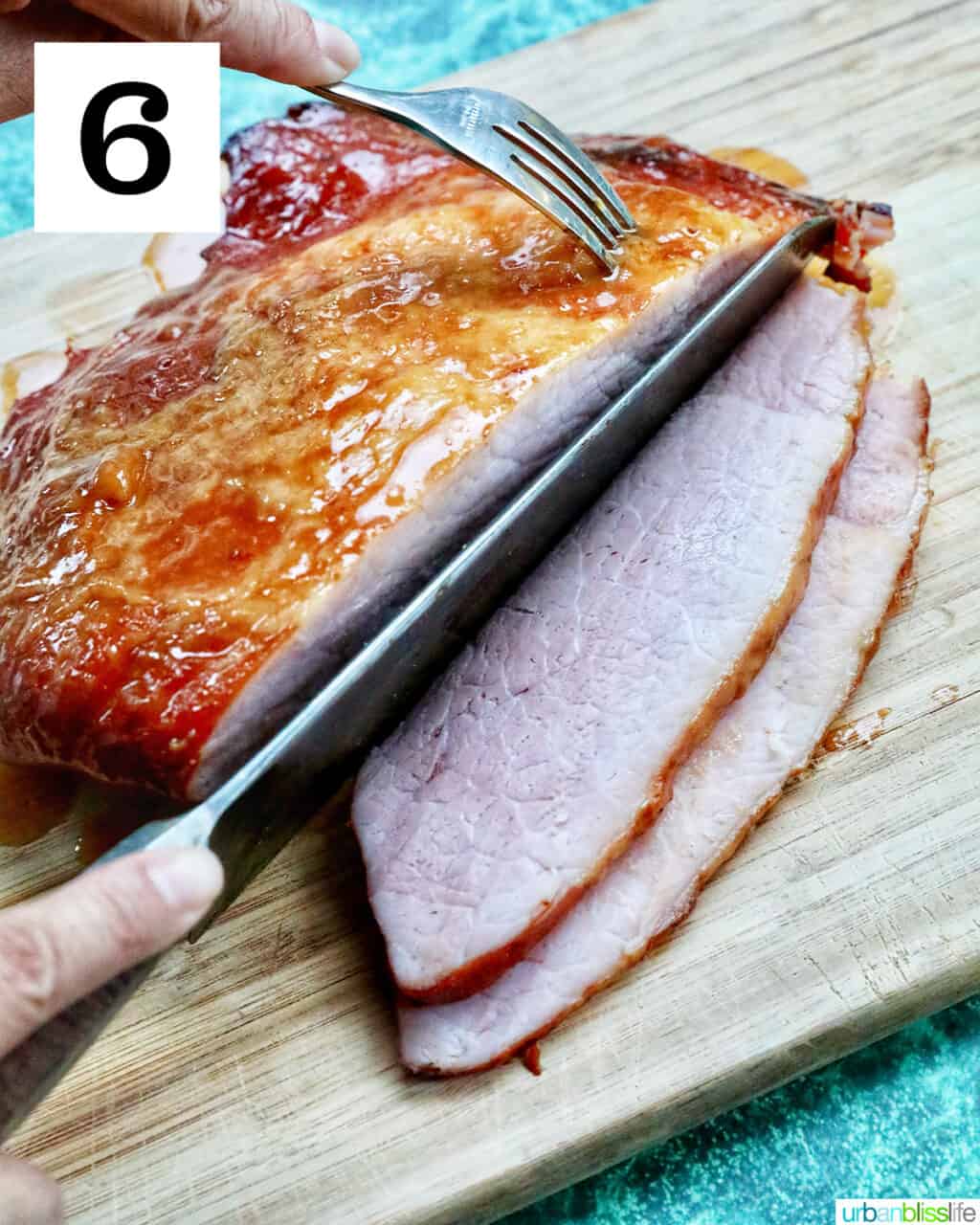 hand with knife slicing glazed ham on a cutting board.