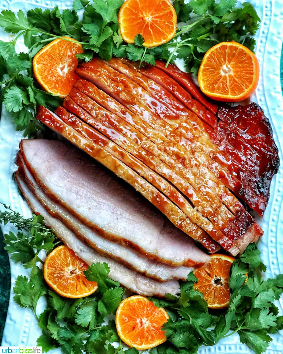sliced honey glazed air fryer ham on a plate with fresh herbs and sliced oranges.