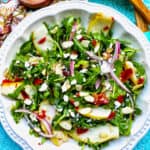 arugula, pears, prosciutto, and red onion salad in a white bowl.