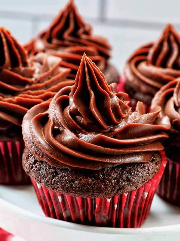 chocolate cupcakes with chocolate fudge frosting stacked on a cake pedestal.