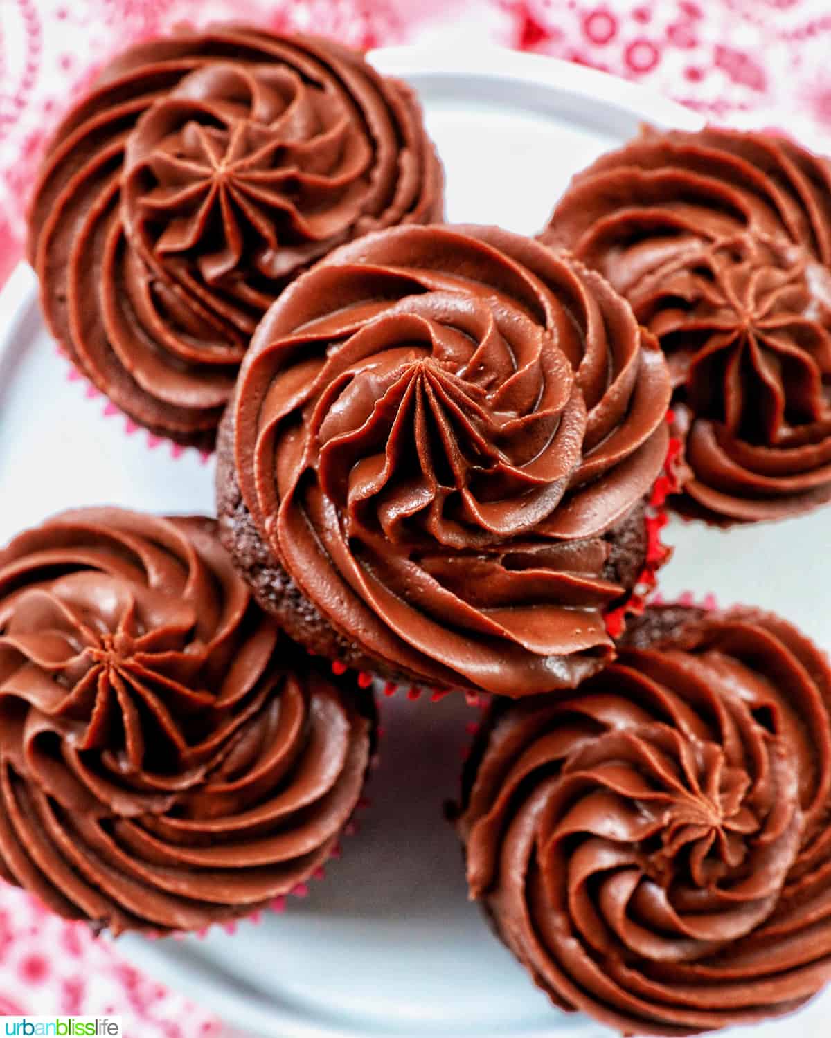 chocolate cupcakes with chocolate fudge frosting stacked on a cake pedestal.