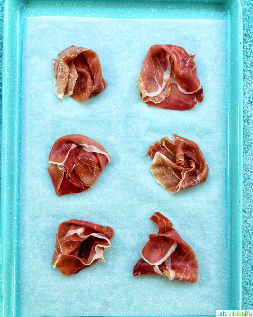 six crispy prosciutto rounds on a blue baking tray.