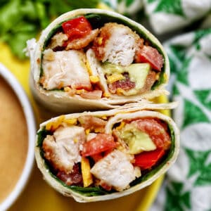 honey mustard chicken wraps sliced in half with the middle exposed next to honey mustard sauce and a green and white patterned napkin.