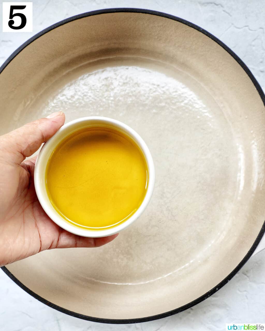 hand adding olive oil in a small bowl to a large skillet.