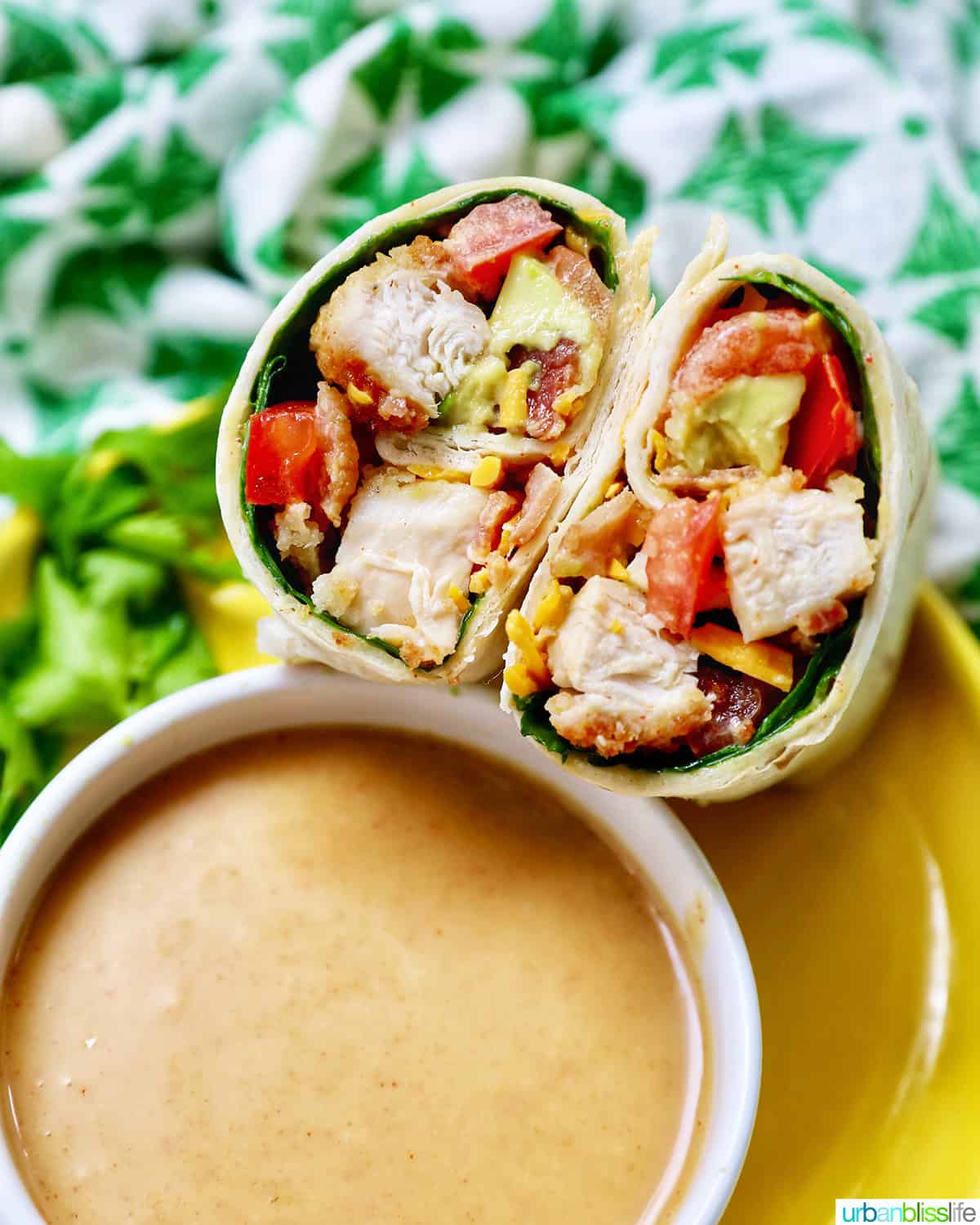 honey mustard chicken wraps sliced in half with the middle exposed next to honey mustard sauce and a green and white patterned napkin.