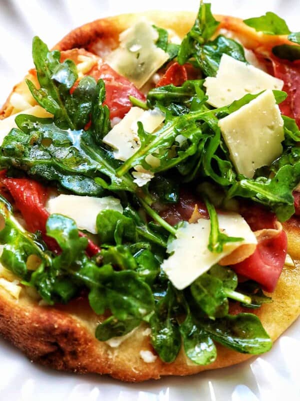 prosciutto flatbread with arugula and parmesan cheese on a scalloped plate.