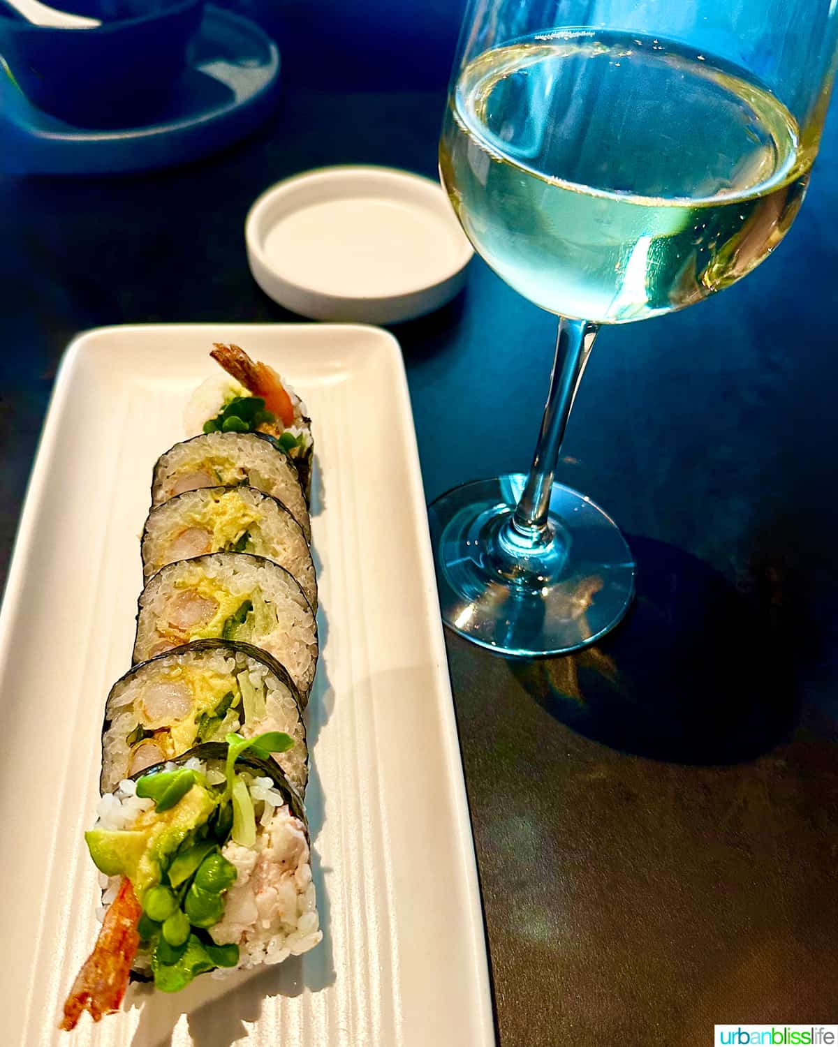 glass of white wine with a plate of sushi rolls.