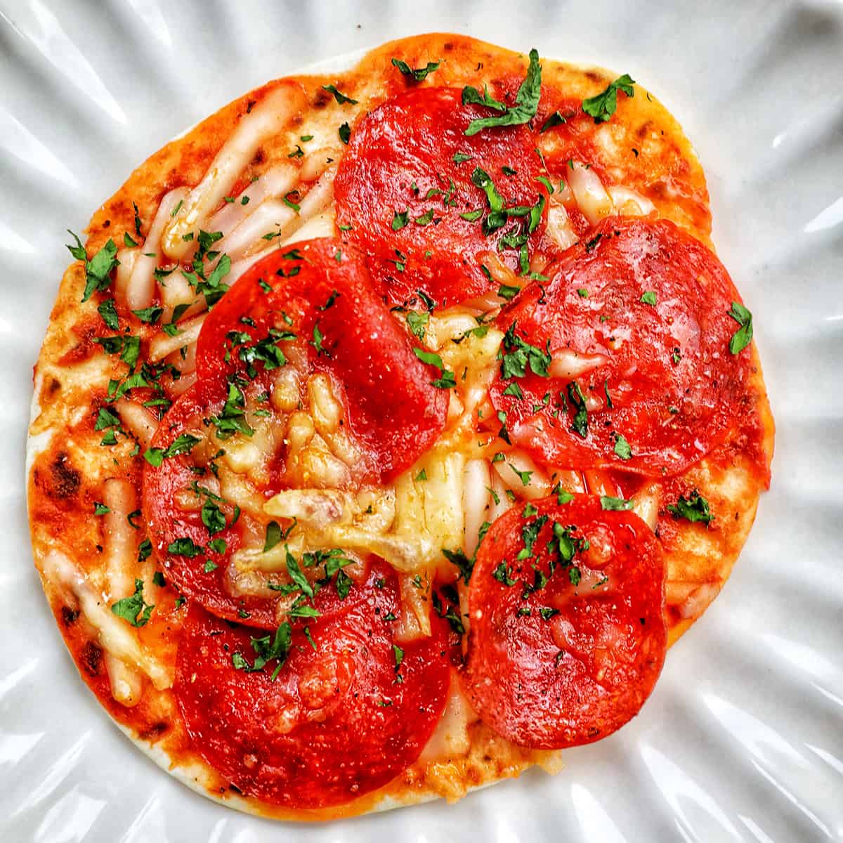 single air fryer mini pepperoni pizza on a scalloped plate.
