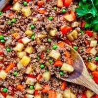 Filipino Beef Giniling (picadillo) in a large pan with a wooden spoon and side of parsley.