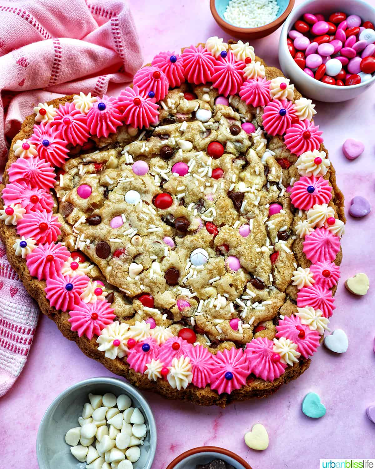 A heart-shaped Valentine's Day cookie cake with pink and white vanilla frosting and red, white, and pink M & M decorations.