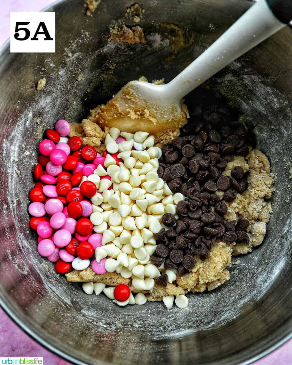 M & Ms, white chocolate chips, and semi-sweet chocolate chips added to batter in a stand mixer bowl.
