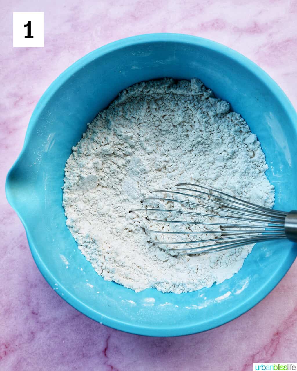 blue bowl with dry baking ingredients and a whisk.
