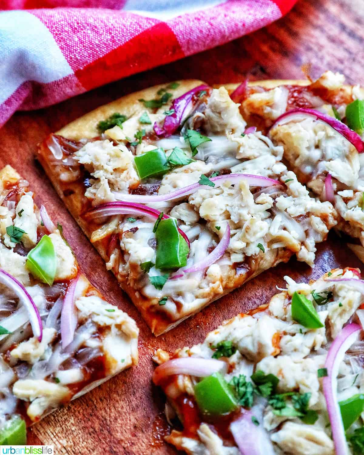 slices of barbecue chicken flatbread pizza with red onions, chicken breast, green peppers, and cilantro.