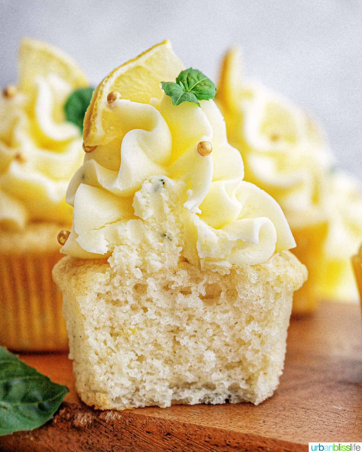 lemon basil cupcake sliced in half with lemon buttercream frosting and garnish of basil leaves and lemon slice.