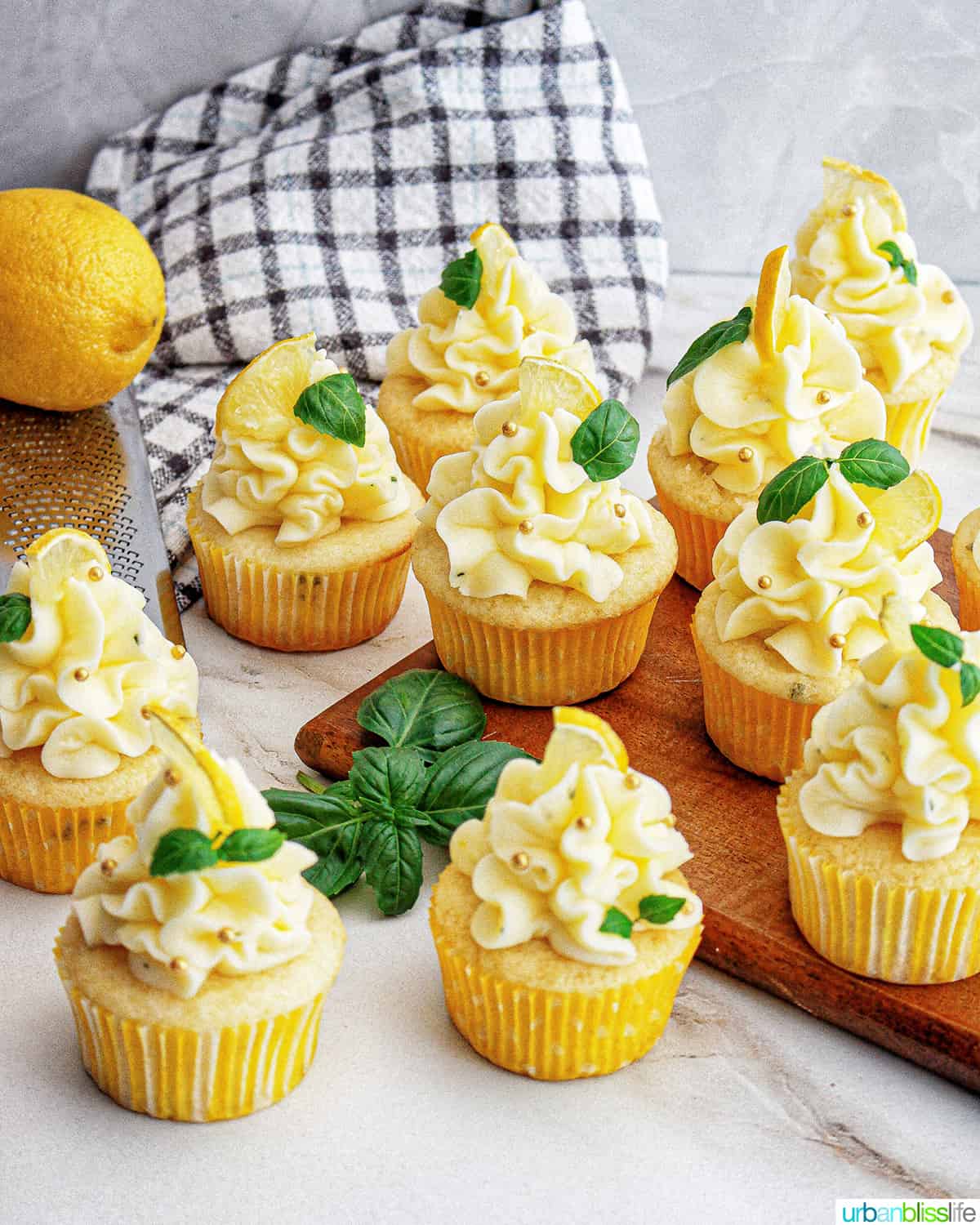 group of lemon basil cupcakes with lemon buttercream frosting and garnish of basil leaves and lemon slice.