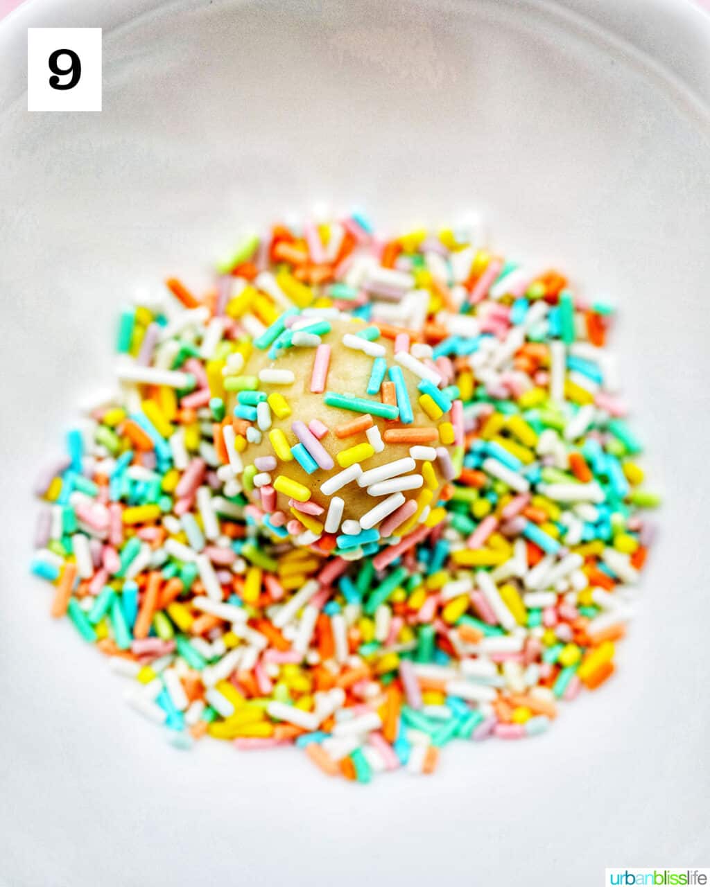 almond sugar cookie dough ball rolled in a bowl of pastel colored sprinkles.