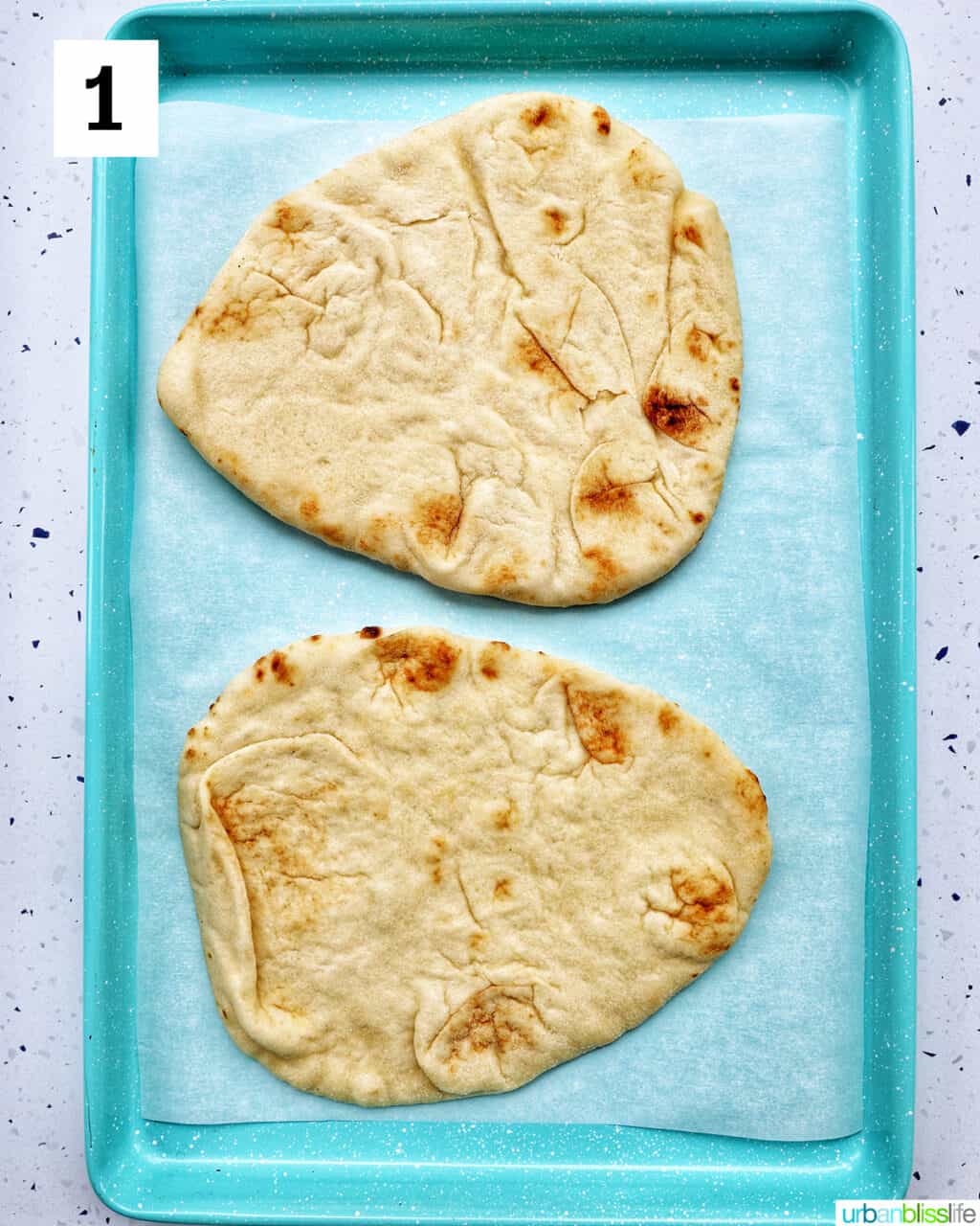 two naan flatbreads on a baking sheet.