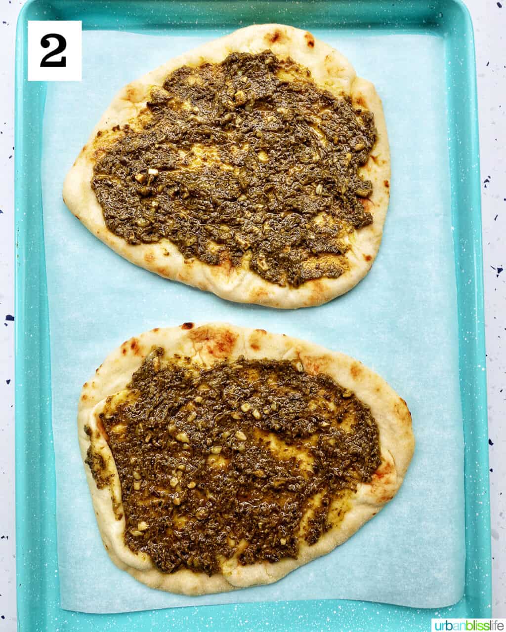 two naan flatbreads with pesto on a baking sheet.