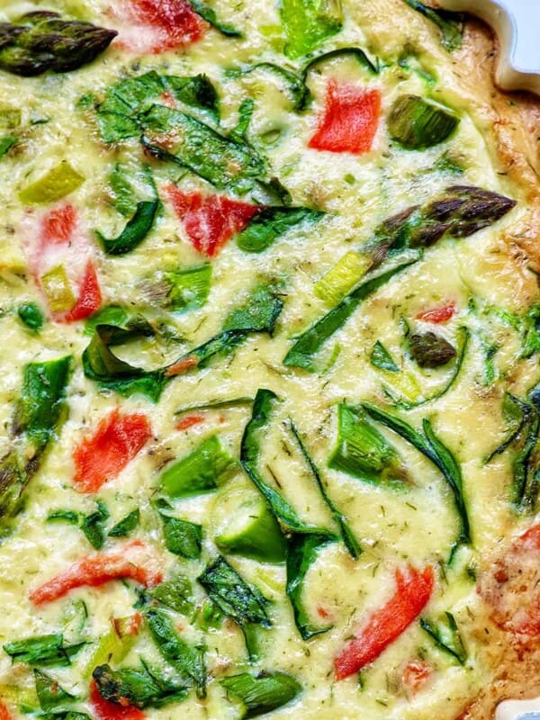Half of a quiche in a pie pan with salmon, asparagus, and leeks.