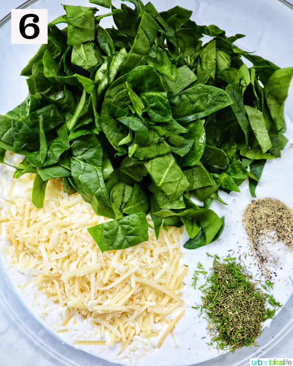 bowl with sliced spinach, shredded cheese, and herbs and seasonings.