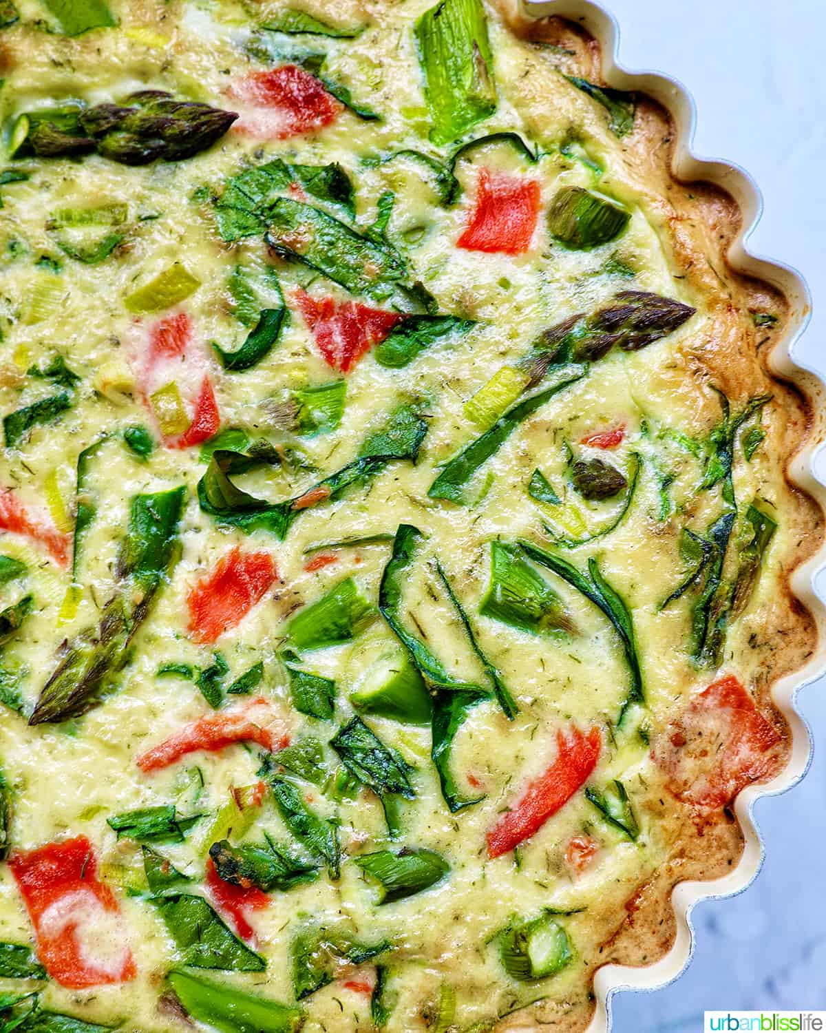 Half of a quiche in a pie pan with salmon, asparagus, and leeks.