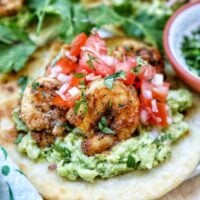 pico de gallo, shrimp, and guacamole on a tortilla with cilantro leaves on the side.