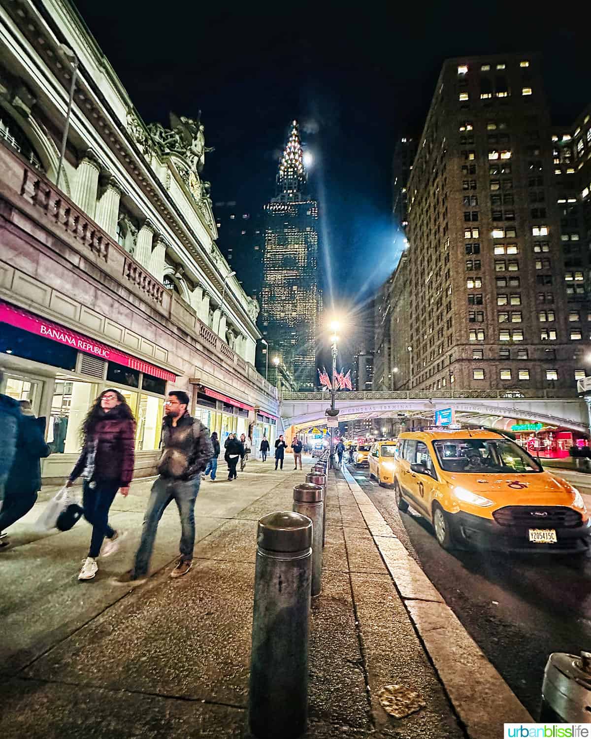 New York City street scene at night with yellow cabs and Chrysler building in the background.
