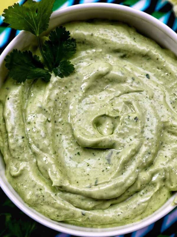 bowl of avocado cilantro lime crema on a colorful modern napkin with garnish of cilantro leaves.