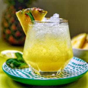 glass of pineapple mocktail with mint leaves and pineapple slice garnish.