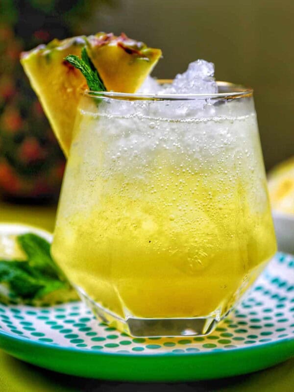 glass of pineapple mocktail with mint leaves and pineapple slice garnish.